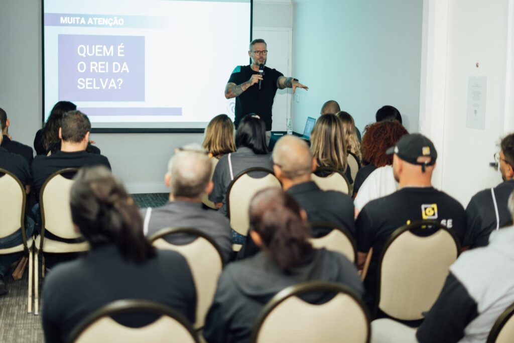 Treinador comportamental O Reprogramador conduzindo palestra para sala cheia, em frente a um slide com a frase “Quem é o rei da selva?”, enquanto o público acompanha atento.