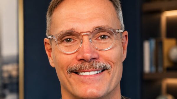 Retrato de homem em ambiente corporativo escuro, usando jaqueta de couro preta e camisa preta, com fundo desfocado e postura séria.